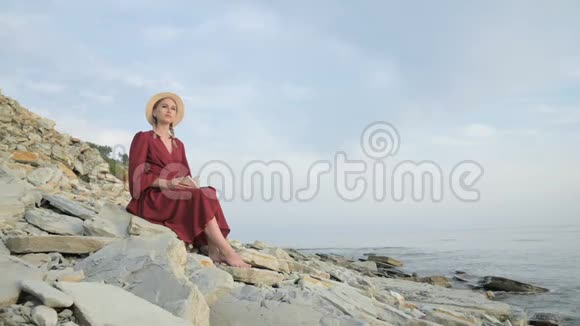 一位穿着夏红色连衣裙和草帽抱着一本书坐在她怀里的白人女孩的肖像视频的预览图