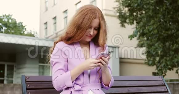 有雀斑的红发女孩晚上在户外的智能手机上写信息视频的预览图