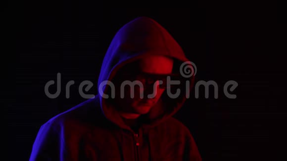 戴着墨镜和引擎盖的男人在黑暗中使用智能手机视频的预览图