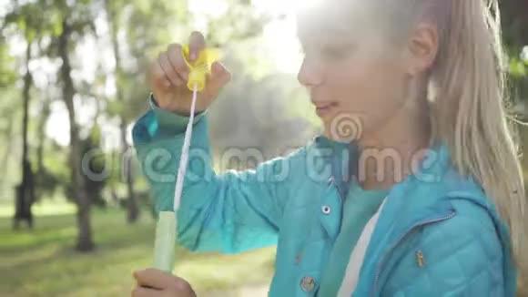 年轻的白种人微笑的金发女孩在阳光明媚的公园里吹肥皂泡穿着休闲服装的年轻积极女士视频的预览图