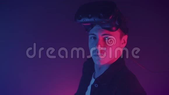 一幅年轻英俊的白种人肖像戴着VR眼镜看着站在霓虹灯背景上的摄像机视频的预览图