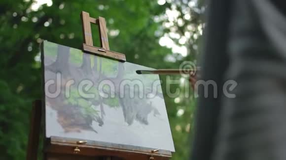 手里拿着画笔的女孩在三脚架上画着一个湖和一棵树视频的预览图