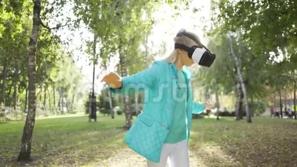 年轻的金发白种人女孩戴着VR眼镜花时间在阳光明媚的公园里穿着虚拟护目镜的青少年视频的预览图