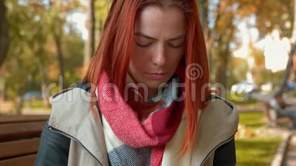 在阳光明媚的天气里长着狐臭头发的女孩坐在长凳上用平板电脑或手机并在网上订购视频的预览图