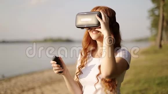 带耳机的VR眼镜里的雀斑红发女孩正在使用遥控器观看360度视频视频的预览图