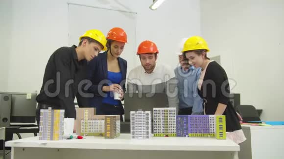 戴着头盔的建筑师看着电脑讨论一个项目和房屋模型视频的预览图