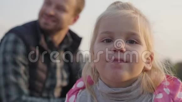一个金发棕色眼睛的小女孩的特写脸看着相机可爱的孩子坐着视频的预览图