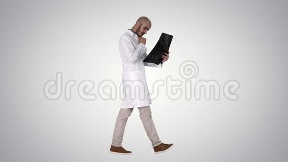 年轻的男性医生在梯度背景下行走时阅读和复习MRI脑扫描视频的预览图