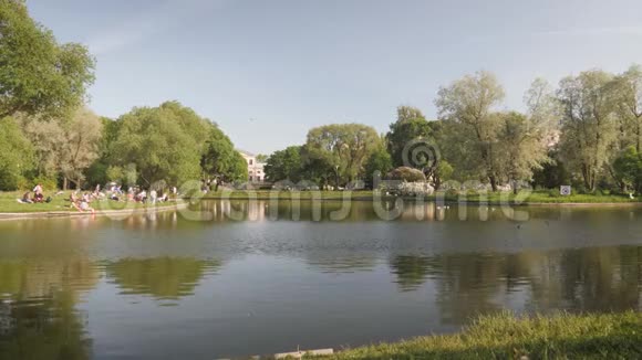 一个人坐在池塘岸边的一个夏季公园里人们在池塘里放松视频的预览图