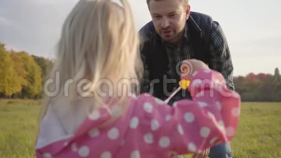 可爱的金发女孩穿着粉红色的点缀夹克和她父亲在户外玩肥皂泡小白种人儿童视频的预览图