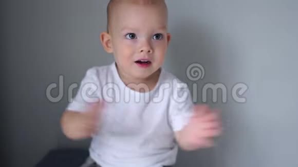 一个穿白色T恤的漂亮蓝眼睛蹒跚学步的男孩的肖像孩子拍手快乐的童年孩子们情绪视频的预览图