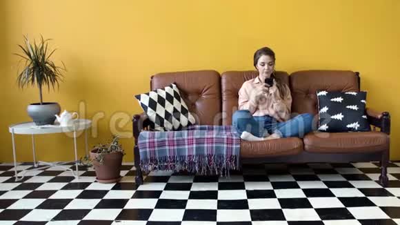 年轻迷人的女人在手机上输入情感信息库存录像年轻女子坐在沙发上快速打字视频的预览图