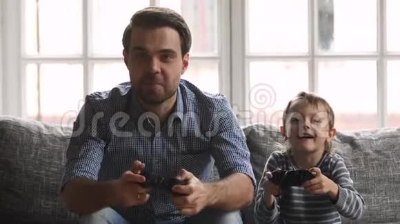 快乐的爸爸和儿子拿着操纵杆在沙发上玩游戏视频的预览图