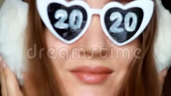 戴眼镜的女人戴着2020年的数字和冬天的耳机新年圣诞节女孩微笑着看着镜头视频的预览图