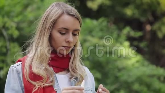 穿着红色围巾喷鼻喷雾的年轻女子站在城市公园保健治疗概念概念视频的预览图