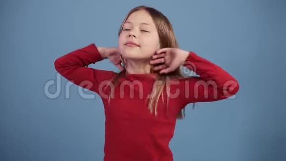 可爱的长发女孩在蓝色背景上微笑和愚弄周围和开玩笑跳舞穿着红色毛衣慢点视频的预览图