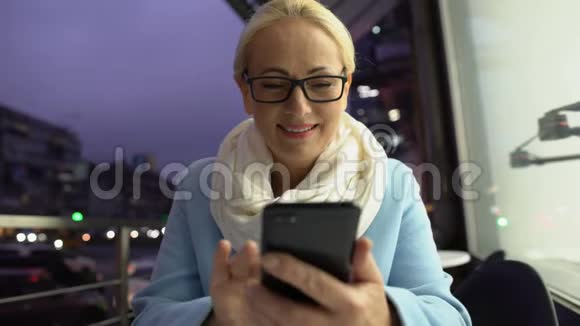 美丽的成熟女人坐在露天露台上用智能手机聊天晚上视频的预览图