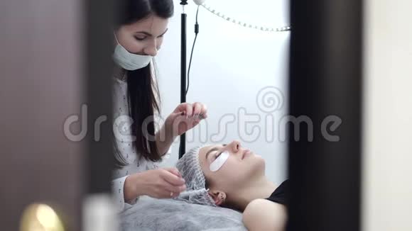 一位身穿一次性面具的深色欧洲睫毛艺术家正在做睫毛的分层视频的预览图