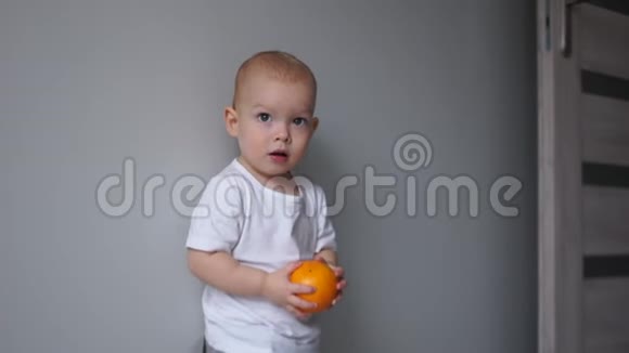 一个可爱的婴儿穿着白色t恤手里拿着一个橘子的肖像孩子笑着扔了一个橘子健康视频的预览图