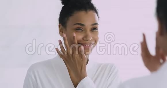 快乐的年轻非洲女人涂面霜照镜子视频的预览图