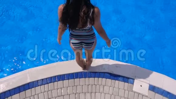 女孩跳到蓝色游泳池慢动作鸟瞰视频的预览图