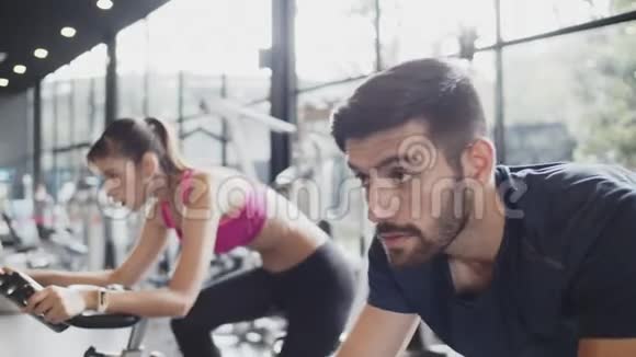 美丽的亚洲女人和高加索男人在健身健身房的固定自行车机上锻炼室内锻炼概念视频的预览图