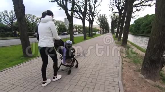 母亲带着婴儿车沿着城市的堤岸散步视频的预览图