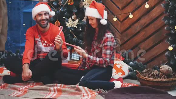 现场视频年轻人穿着红色衣服和圣诞帽在圣诞气氛中与美味的糖果打架视频的预览图