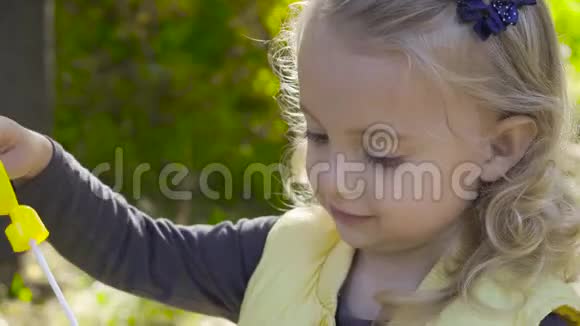 一个迷人的金发女孩的特写吹着肥皂泡微笑着一个棕色眼睛的小孩在公园里玩视频的预览图