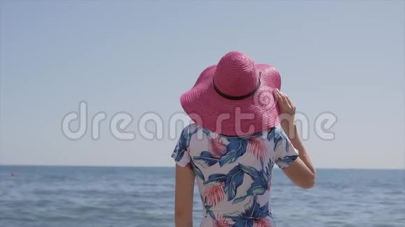 孤独优雅的女人穿着蓝色的泳衣粉红色的帽子站在海边看着地平线视频的预览图
