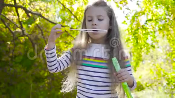 美丽的黑发女孩留在秋天的阳光和吹肥皂泡穿条纹夹克的小孩在玩视频的预览图
