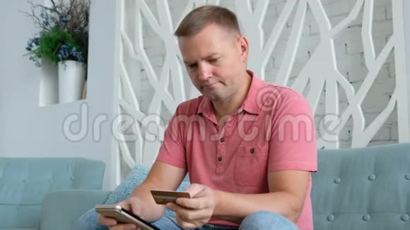 年轻的白种人使用智能手机在客厅里用信用卡进行网上购物视频的预览图