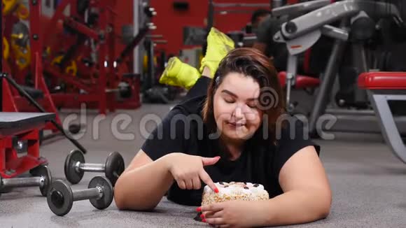 缺乏意志力饮食健身医疗保健肥胖的年轻女性在健身房里与蛋糕欲望作斗争的肖像体育运动视频的预览图