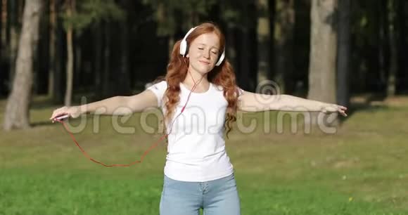 戴着白色耳机的红发雀斑女孩正像一只鸟儿挥动着双手闭着眼睛跳舞视频的预览图