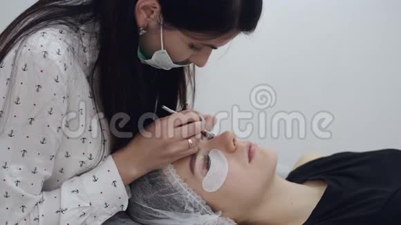 一位穿着一次性面具的深色欧洲睫毛艺术家正在做睫毛的分层视频的预览图