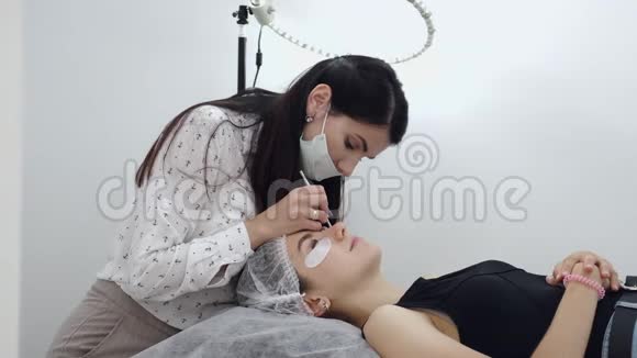 一位穿着一次性面具的深色欧洲睫毛艺术家正在做睫毛的分层视频的预览图