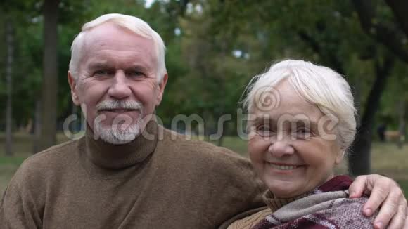微笑成熟的夫妇坐在公园的长凳上拥抱社保视频的预览图