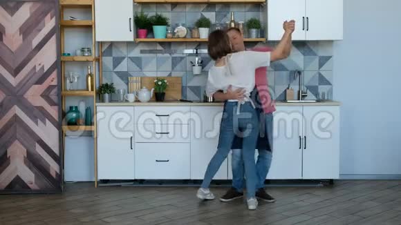 新婚夫妇快乐地在家厨房里跳舞听音乐爱玩视频的预览图