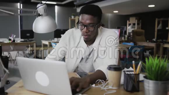 美国黑人年轻人在笔记本电脑上工作在办公室使用电话视频的预览图