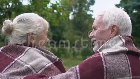 成熟的一对夫妇坐在公园的长凳上在格子布下取暖后景视频的预览图