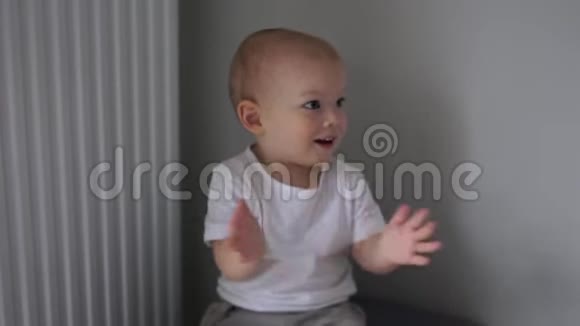 可爱的两岁婴儿穿着白色T恤坐在椅子上在室内拍手快乐的童年视频的预览图