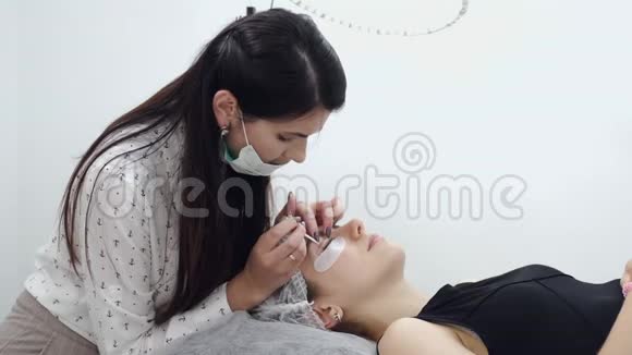 一个棕色皮肤的欧洲睫毛师戴着一次性口罩正在做睫毛的分层视频的预览图