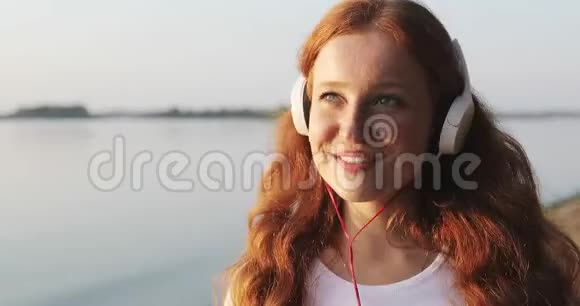 戴着白耳机的红头发雀斑女孩的脸上挂满了听歌和微笑视频的预览图