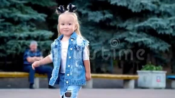 一个穿着时髦牛仔西装头上扎着马尾辫的小女孩穿过公园视频的预览图