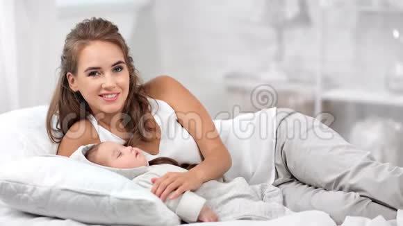 微笑关爱的母亲摆着睡懒觉可爱的婴儿拥抱和触摸感觉爱中镜头视频的预览图