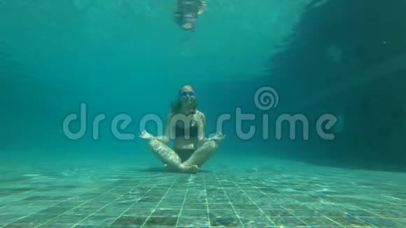 慢动作水下拍摄一位年轻女子在瑜伽姿势冥想游泳池底部的概念视频的预览图