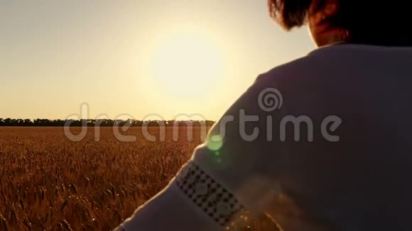 穿着白色连衣裙的年轻女子在日落的背景下穿过一片麦田视频的预览图