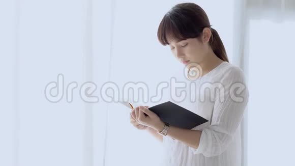 美丽的肖像年轻的亚洲女人站着看书在家里的卧室里考试压力很大视频的预览图