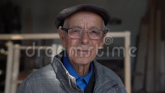 一位老木匠戴着蓝色衬衫灰色夹克和帽子的眼镜蓝眼睛盯着一个看着视频的预览图
