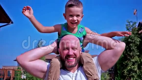 儿子和父亲的肖像孩子坐在父亲的肩膀上幸福的家庭在欢笑视频的预览图